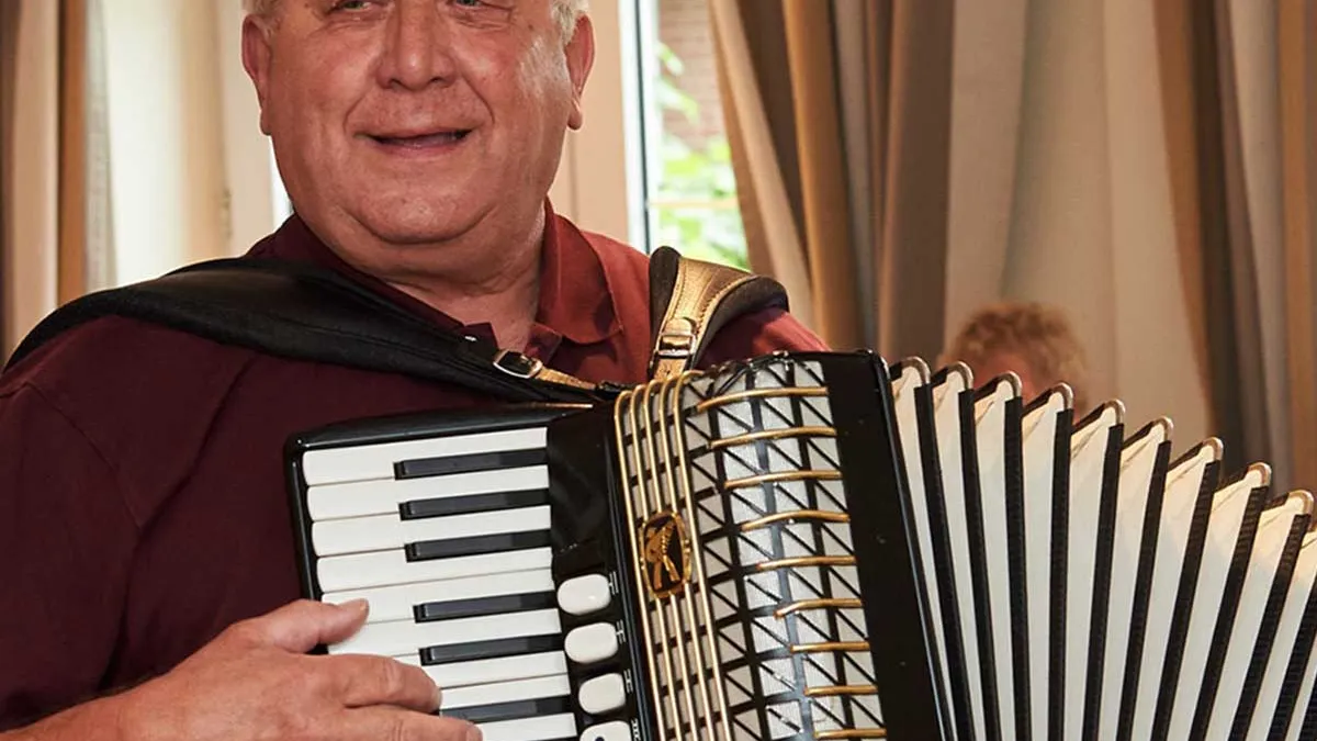 Bewohner von PFLEGEN & WOHNEN HAMBURG in Horn spielt lächelnd Akkordeon als Freitzeitaktivität.