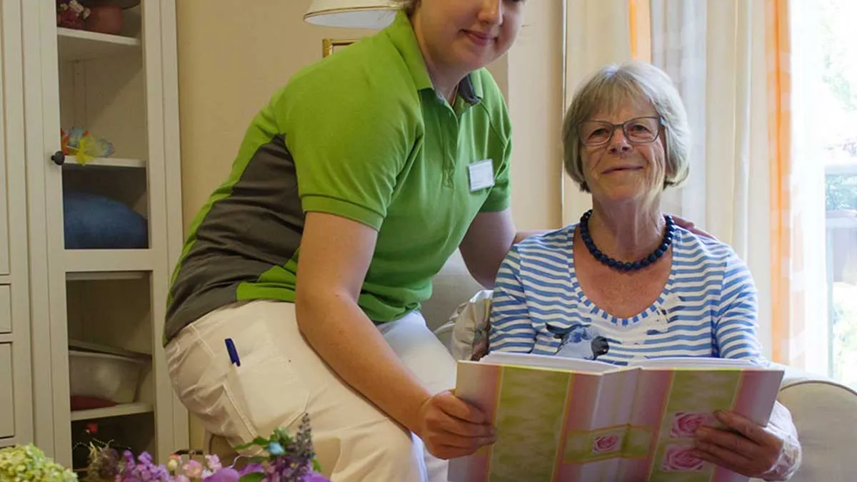 Bewohnerin von PFLEGEN & WOHNEN HAMBURG am Standort Lutherpark zeigt einer Pflegerin Bilder aus ihrem Fotoalbum.