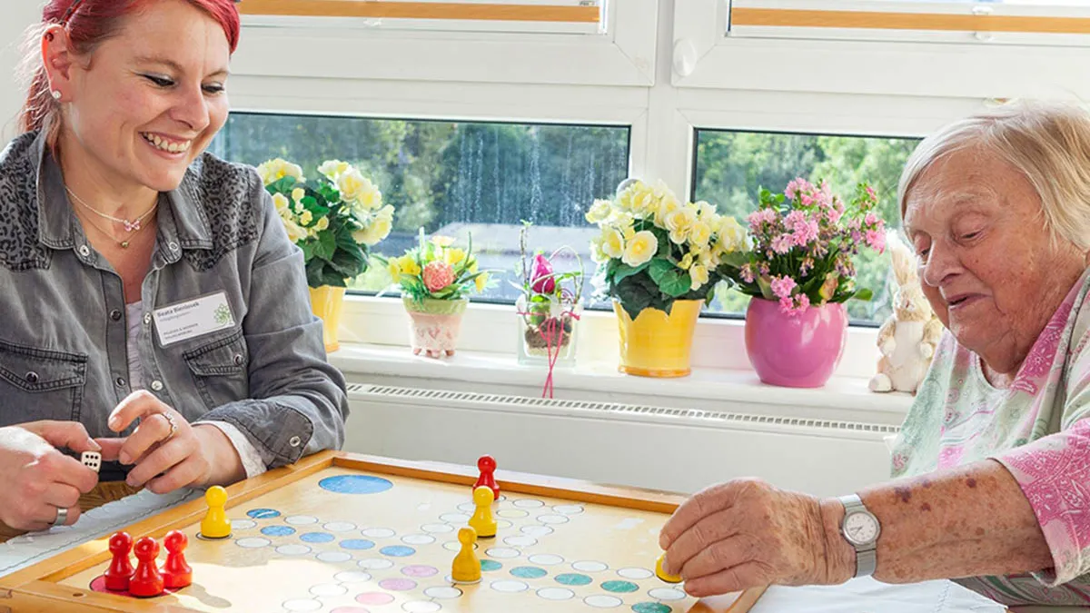 Eine Seniorin in der PFLEGEN & WOHNEN HAMBURG Einrichtung in Wilhelmsburg beim Gesellschaftsspiel spielen mit einer Betreuerin.