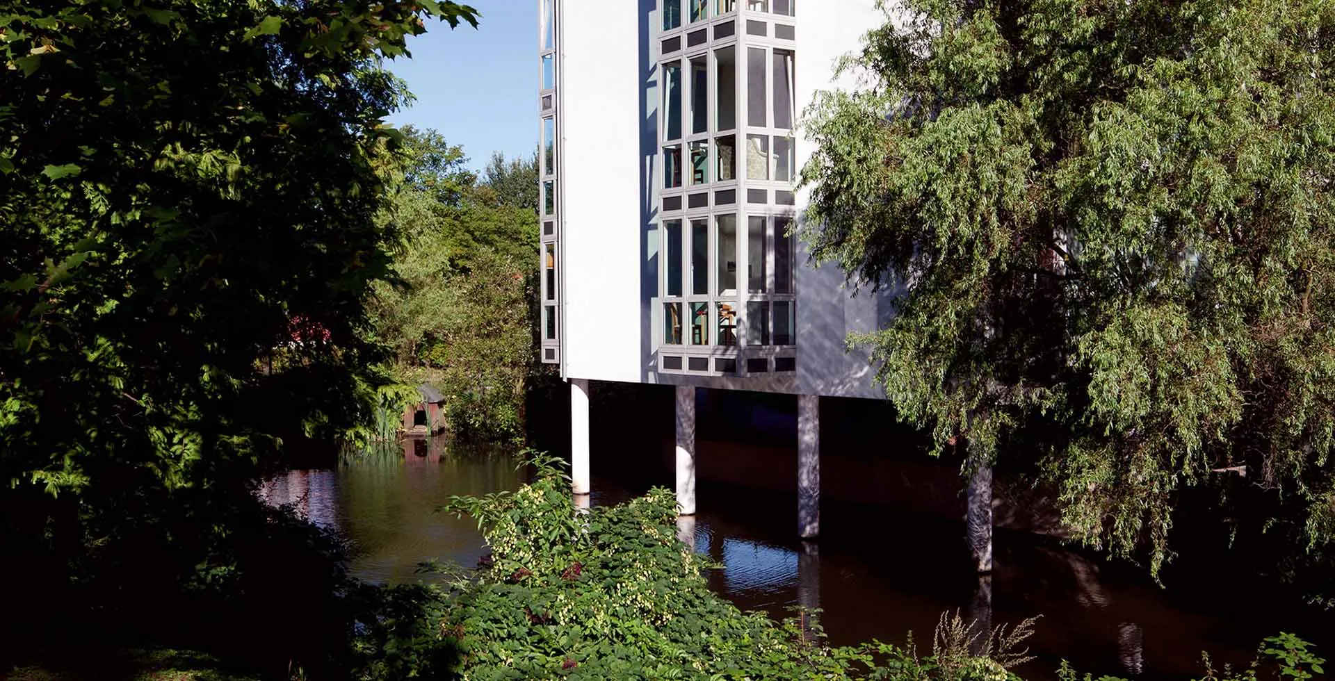 Gebäude von PFLEGEN & WOHNEN HAMBURG Wilhelmsburg auf Säulen über dem Wasser, moderne Einrichtung für Pflege und Betreuung.
