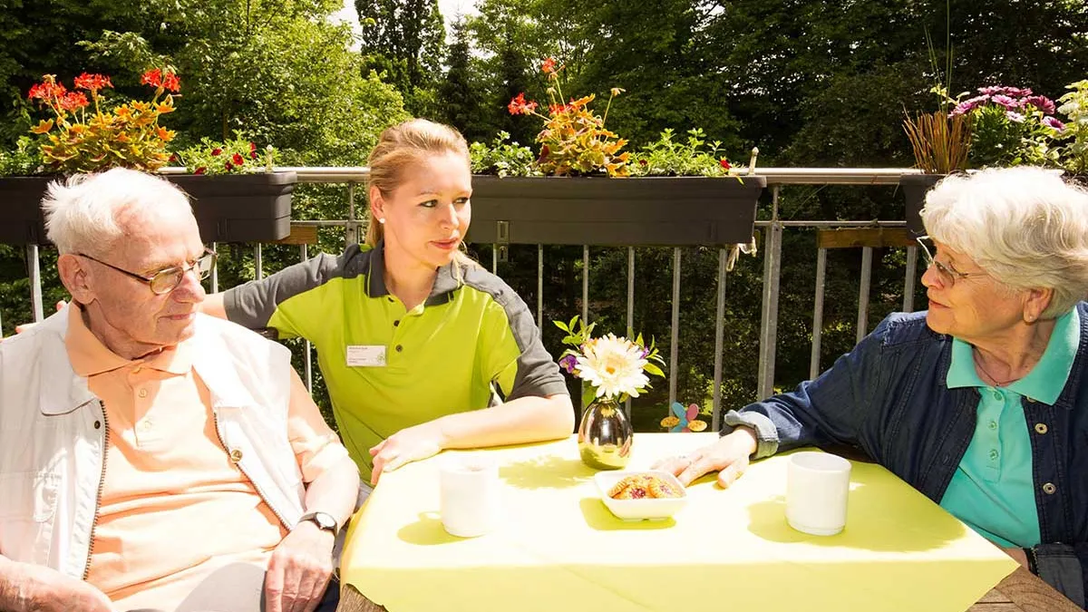 Pflegerin leistet Ehepaar Gesellschaft beim Kaffee im PFLEGEN & WOHNEN HAMBURG-Standort Farmsen.