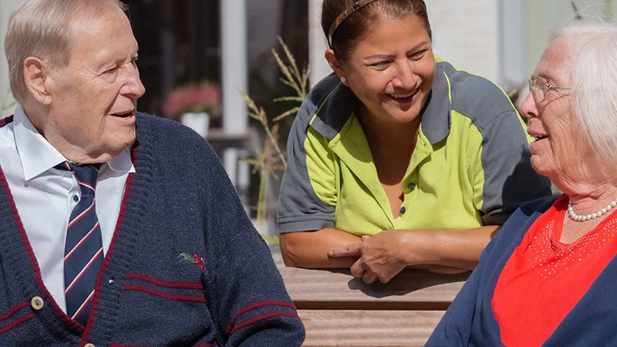 Pflegerin von PFLEGEN & WOHNEN HAMBURG am Standort Marienthal unterhält sich mit zwei Bewohnern.