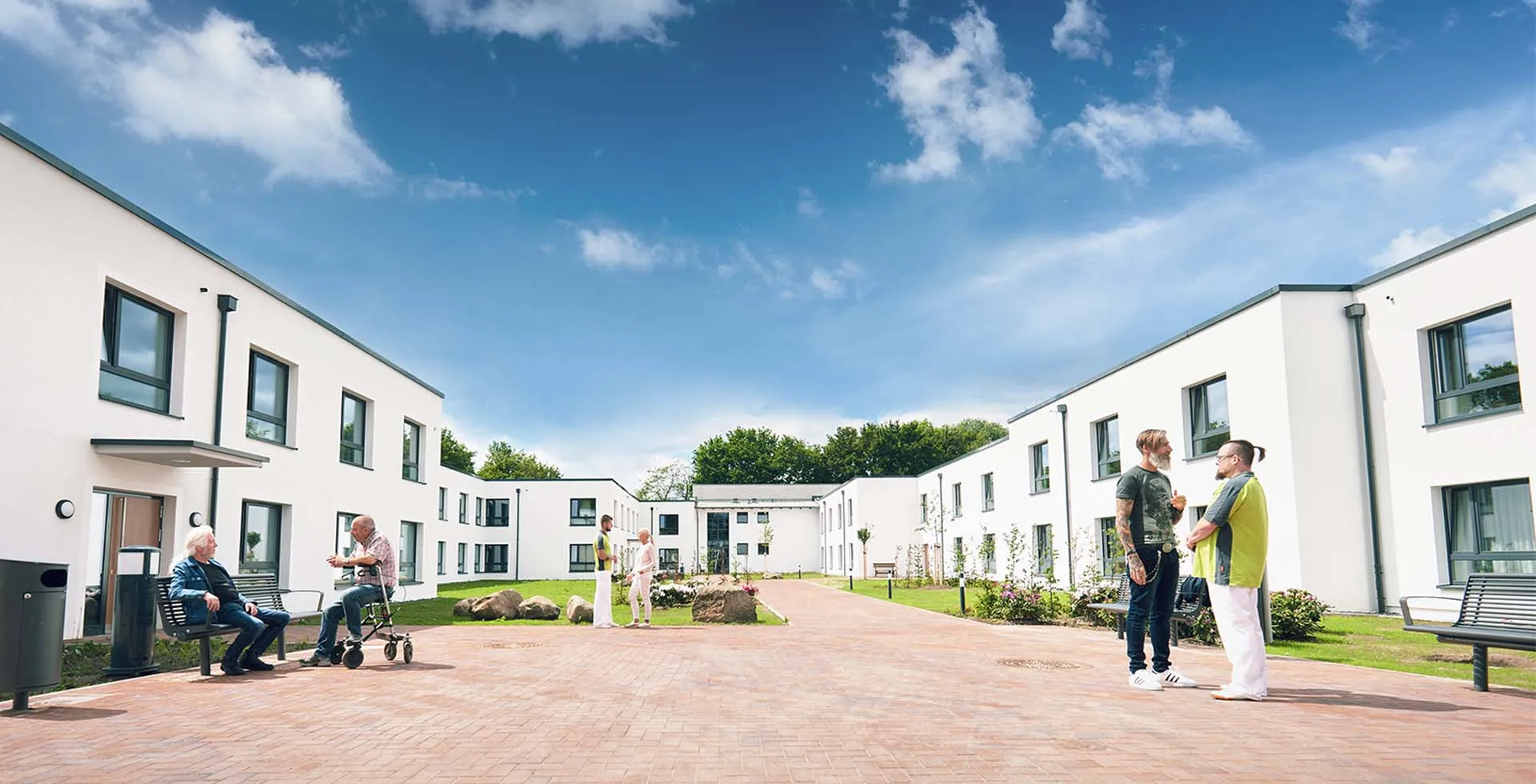 Suchterkrankte Bewohner und Pfleger von PFLEGEN & WOHNEN HAMBURG Öjendorf im begrünten Innenbereich mit Sitzmöglichkeiten.