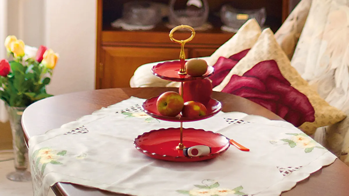 Die Ausstattung in den gepflegten Zimmern mit einem roten Etagere mit Früchten vor einem komfortablen Sofa bei PFLEGEN & WOHNEN HAMBURG Wilhelmsburg.