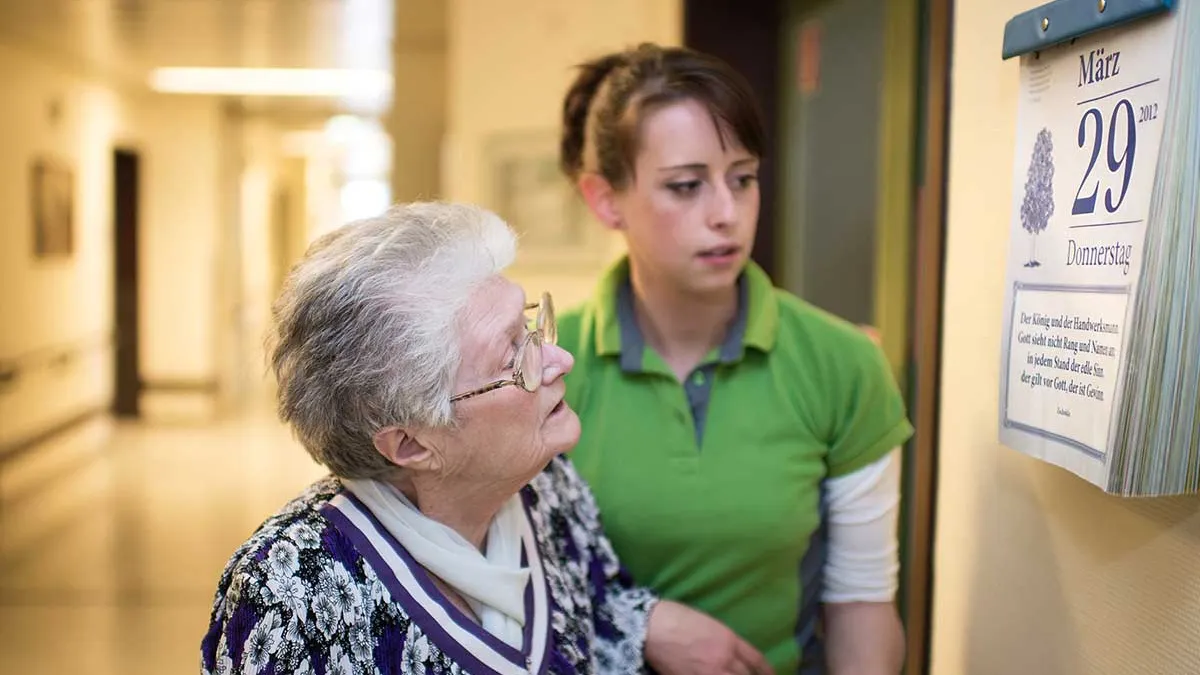 Pflegerin und Bewohnerin schauen gemeinsam auf einen Kalender im Korridor von PFLEGEN & WOHNEN HAMBURG in Horn.