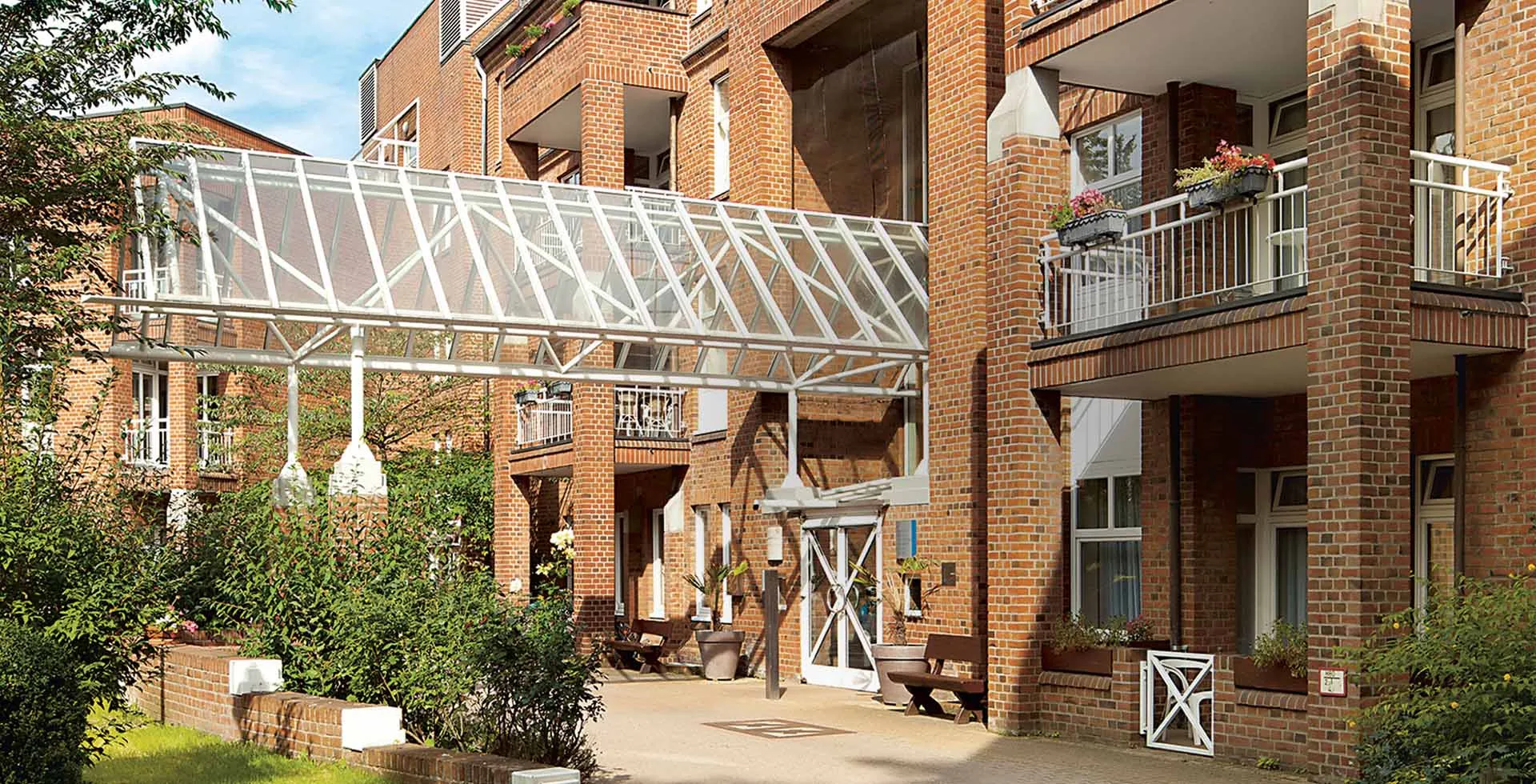 Gebäudeansicht von PFLEGEN & WOHNEN HAMBURG am Standort Altona mit Balkonen, Bepflanzung und einem überdachtem Zugang.