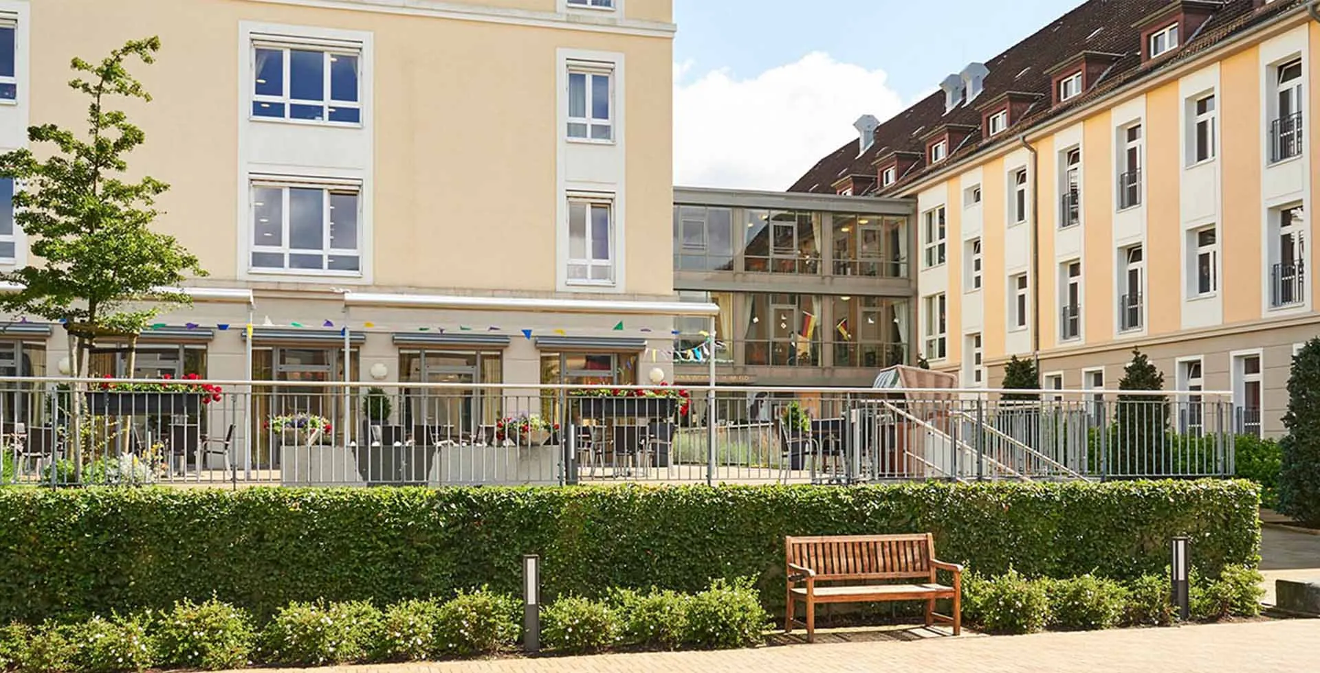 Außenansicht von PFLEGEN & WOHNEN HAMBURG Heimfeld mit Sitzmöglichkeiten zwischen Wohngebiet und Kita, für Pflegebedürftige.