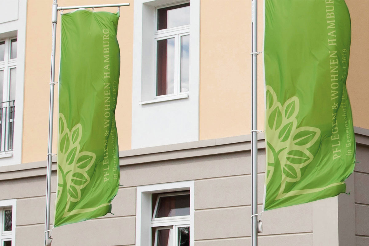 Fahnen wehen am Mast vor dem Hauptgebäude von PFLEGEN & WOHNEN HAMBURG – in den grünen Farben des Logos.