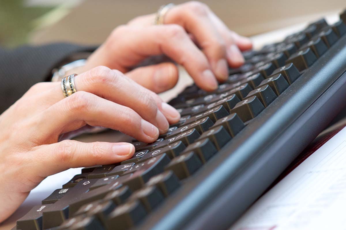 Zwei Hände bedienen die Tastatur, um elektronische Rechnungen am Monitor aufzurufen.