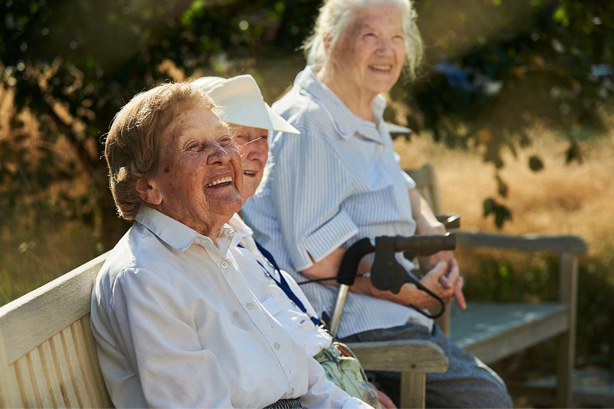 Seniorinnen von PFLEGEN & WOHNEN HAMBURG sitzen gemeinsam auf einer Bank im Garten im geschützten Außenbereich.