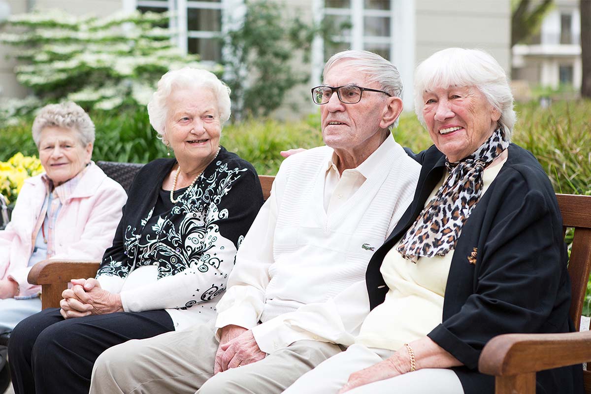 Senioren sitzen im gepflegten Innenhof von PFLEGEN & WOHNEN HAMBURG Finkenau: Betreuung und Pflege in naturnaher Umgebung.