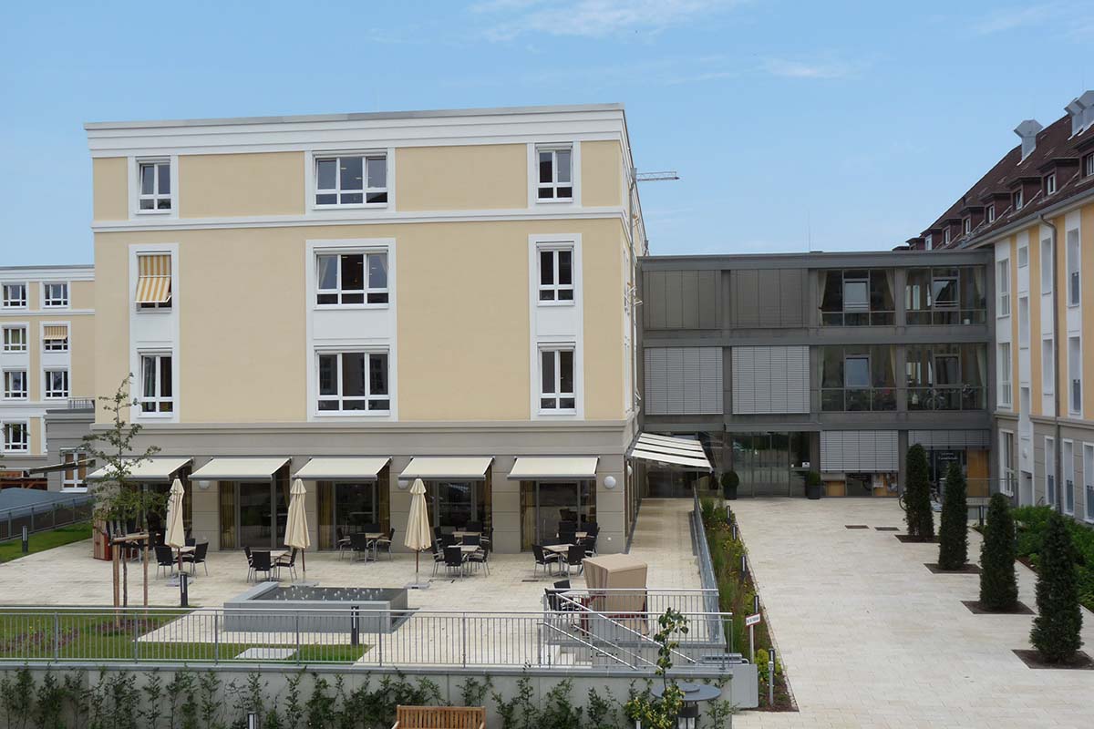 Außenansicht von PFLEGEN & WOHNEN HAMBURG Heimfeld mit modernem Erweiterungsbau, großzügigem Innenhof und Sitzmöglichkeiten.