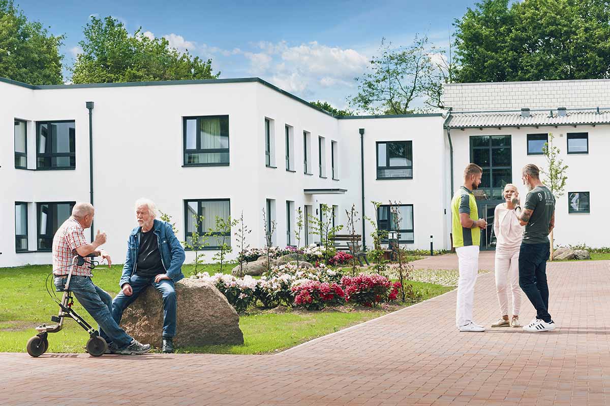 Pfleger und Betreuer mit suchtkranken Bewohnern vor dem modernen Gebäudekomplex von PFLEGEN & WOHNEN HAMBURG Öjendorf.