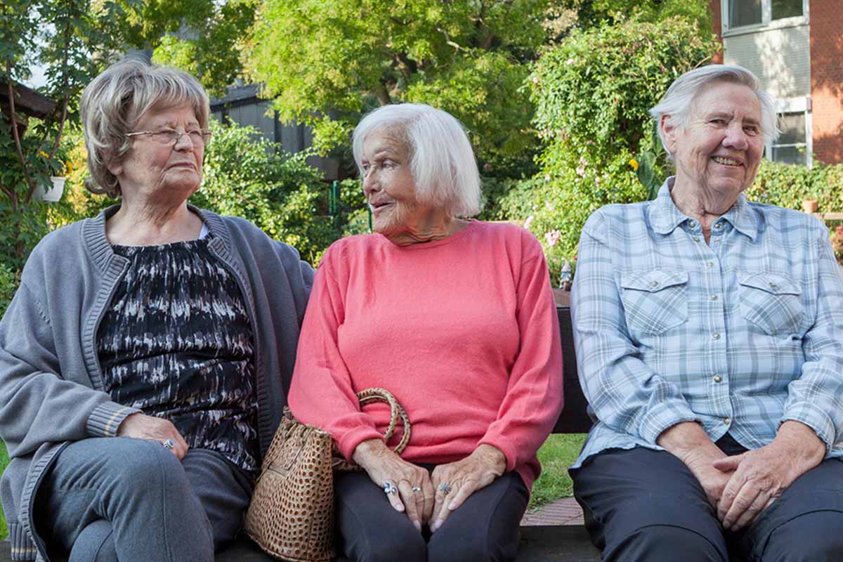 Seniorinnen von PFLEGEN & WOHNEN HAMBURG Wilhelmsburg in Therapie bei freundlichem Austausch auf einer Parkbank im Park.