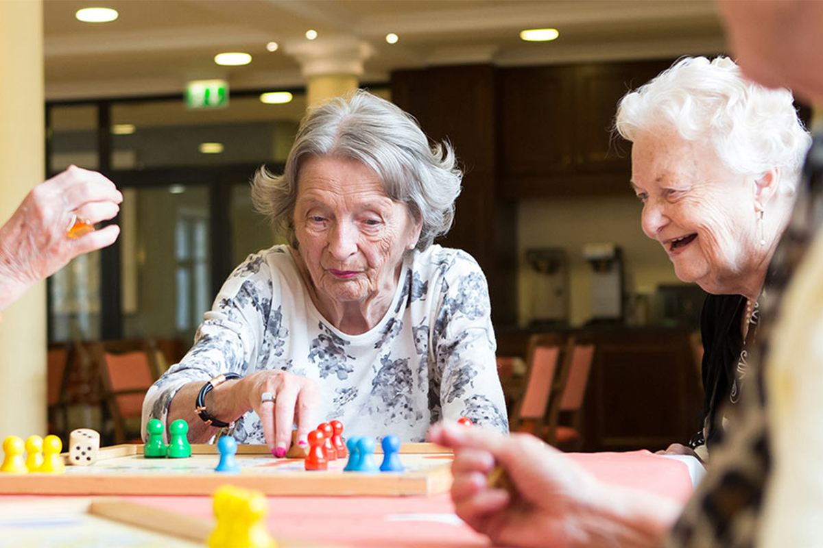 Seniorinnen spielen und lachen im Gemeinschaftsraum von PFLEGEN & WOHNEN HAMBURG.
